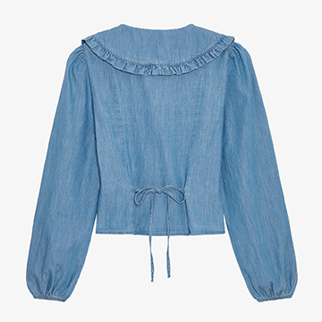 Flat lay product shot showing the back view of a light blue denim blouse with a detailed tie-back closure at the waist.
