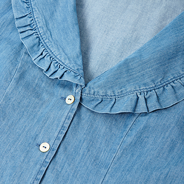 High-resolution close-up detail shot focusing on the ruffled collar, stitching, and button placement of a light blue denim blouse.