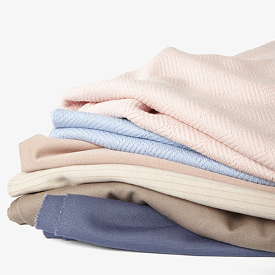A creative still life composition of stacked pastel and neutral fabrics by Yellow Thread Studio in London