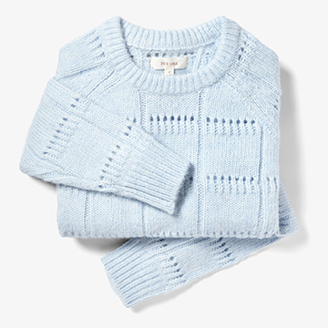 Creative fashion still life photography of a styled and folded knitwear sweater in light blue colour on a crisp white background.