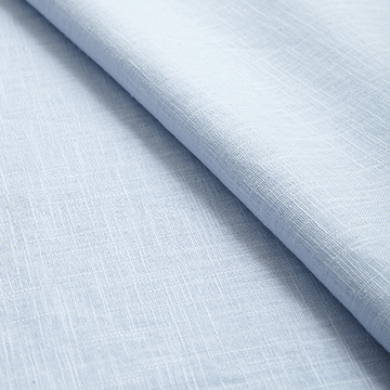Alternative close-up view of folded light blue linen fabric highlighting the soft shadowing and natural weave of the textile.