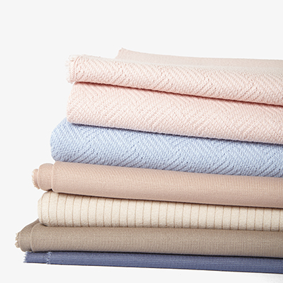 A creative still life composition of stacked pastel and neutral fabrics by Yellow Thread Studio in London