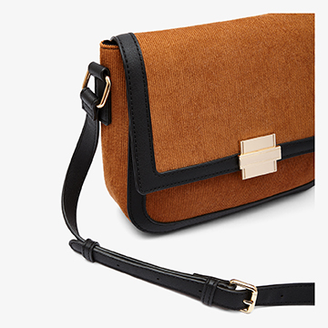Side angle close-up shot of a tan suede handbag showing the depth of the bag and the hardware attachment of the black leather shoulder strap.